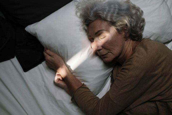 femme âgée cheveux gris qui dort sur le côté avec oreiller et drap blancs