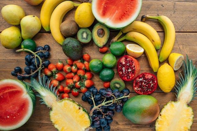 Bananes, poires, ananas coupé en deux, raisin noir, pastèque coupée en deux, fraises, avocats, citrons et citrons verts, grenade coupée en deux sur une table en bois