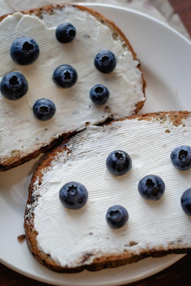 Deux tartines avec fromage blanc étalé et des myrtilles dessus