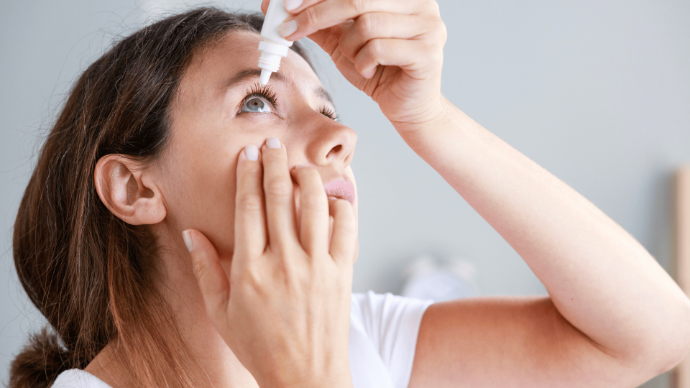 Femme la tête penchée qui tient un flacon blanc au-dessus de son oeil