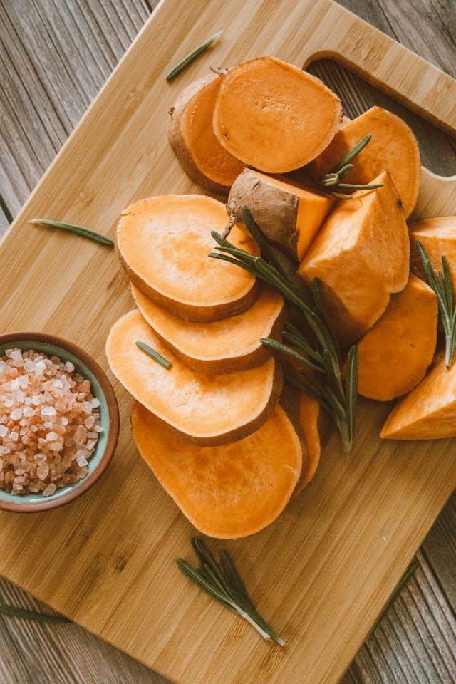 Patates douces crues en rondelles sur une planche en bois avec coupelle de sel rose à côté