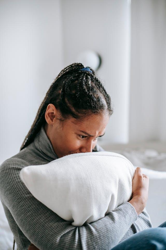 Jeune femme noire stressée avec pull col roulé gris qui serre un oreiller blanc dans ses bras