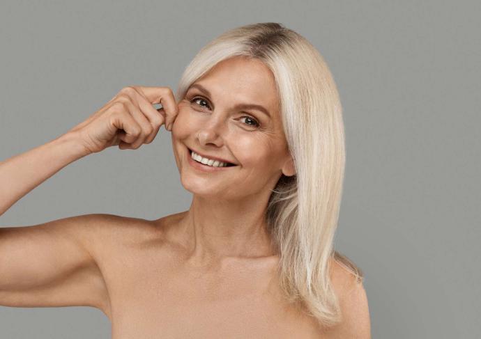Femme blonde 50 ans qui sourit en pinçant sa joue avec une main