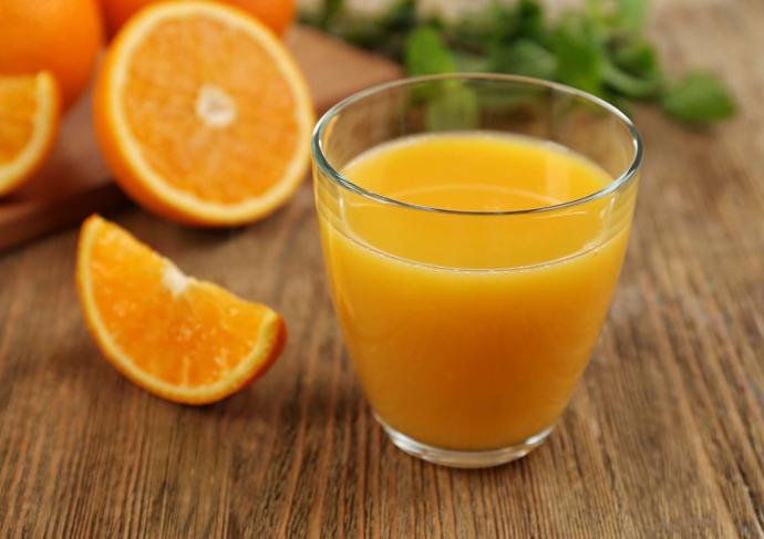 Jus d'orange dans un verre avec des quartiers d'orange à côté et en arrière-plan sut une table en bois