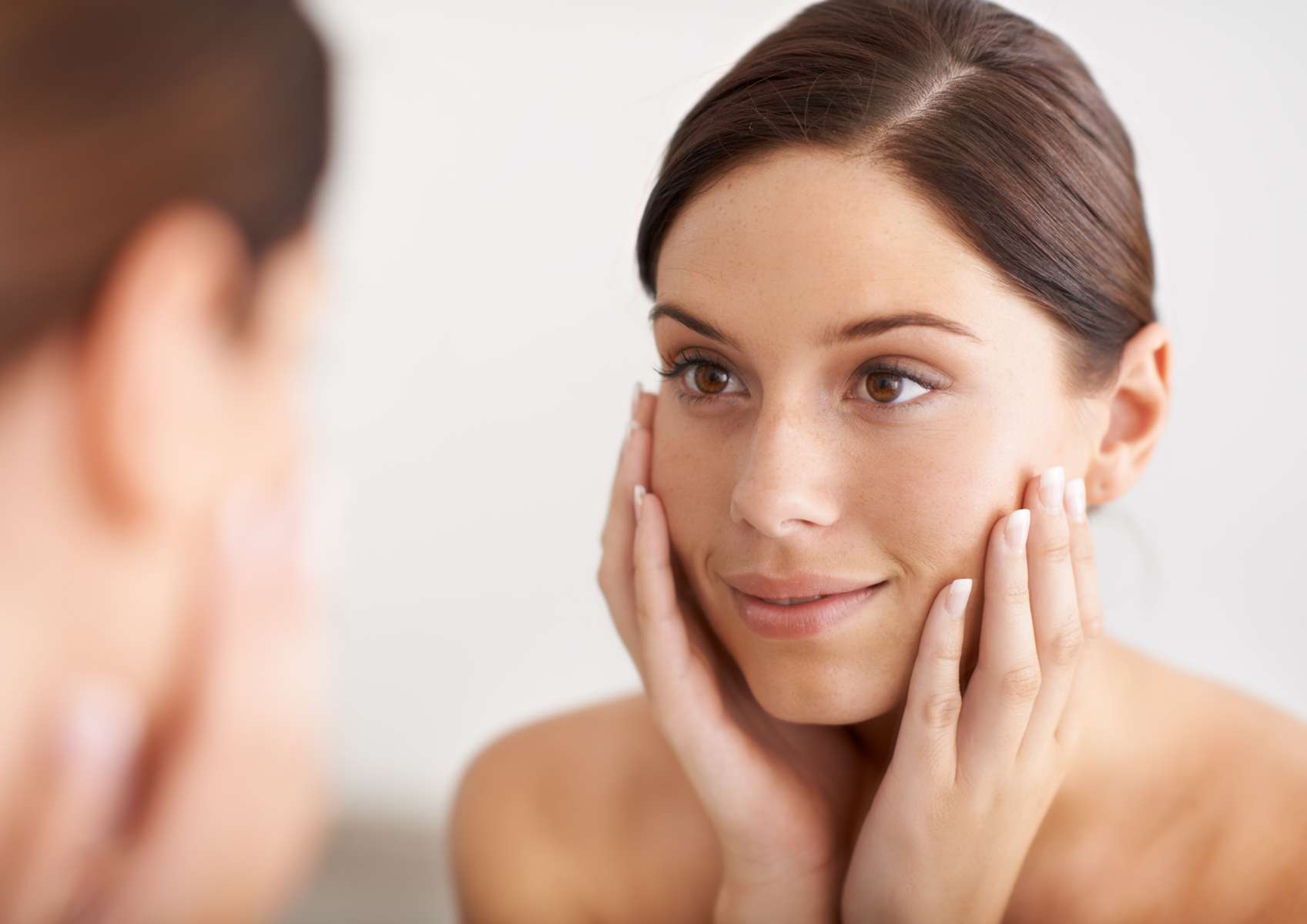 Jeune femme qui sourit devant le miroir avec les mains en coupe sur ses joues