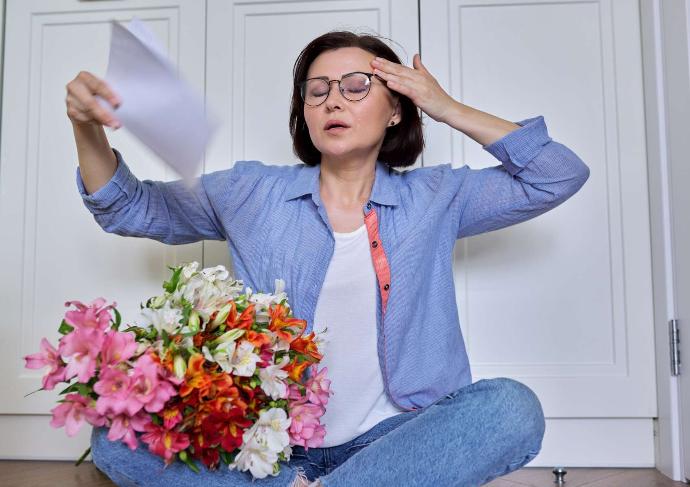 Femme assise en tailleur avec bouquet de fleurs sur les genoux qui s'évente avec une feuille