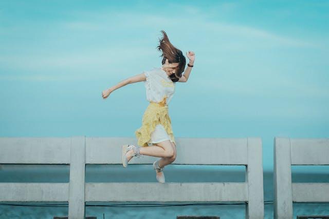 Femme qui saute en souriant devant barrière et mer