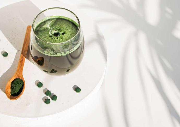 Spiruline liquide dans un verre, en poudre dans une cuillère en bois et en comprimés