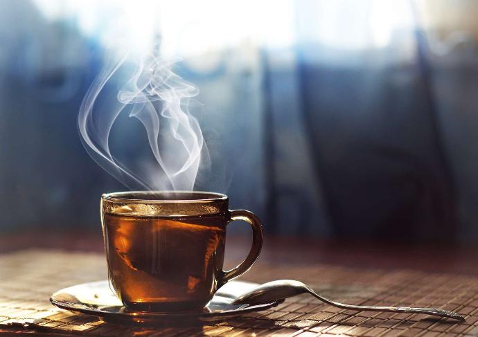 Tasse de thé fumante sur soucoupe et petite cuillère posée dessus avec en arrière-plan rais de lumière