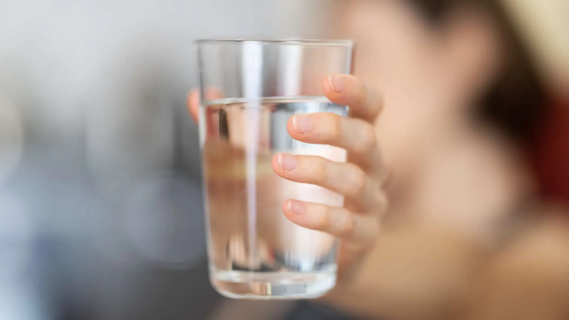 Verre d'eau en gros plan tenue par main de femme en arrière-plan flou